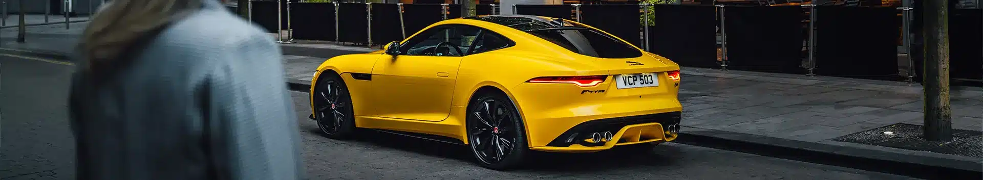 Yellow sports car parked on a city street, sleek design, rear view highlights dual exhaust.