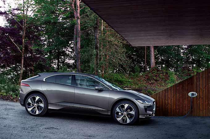 Electric car charging at a home station with a wooded backdrop, showcasing eco-friendly technology.