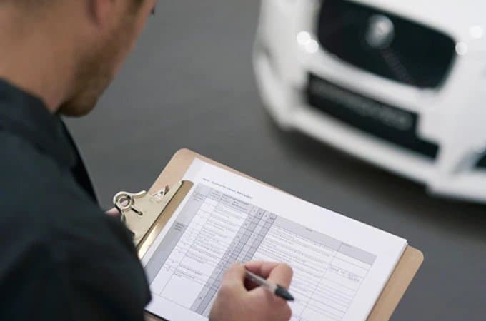 Man filling out a checklist on a clipboard in front of a white car, possibly during an inspection.