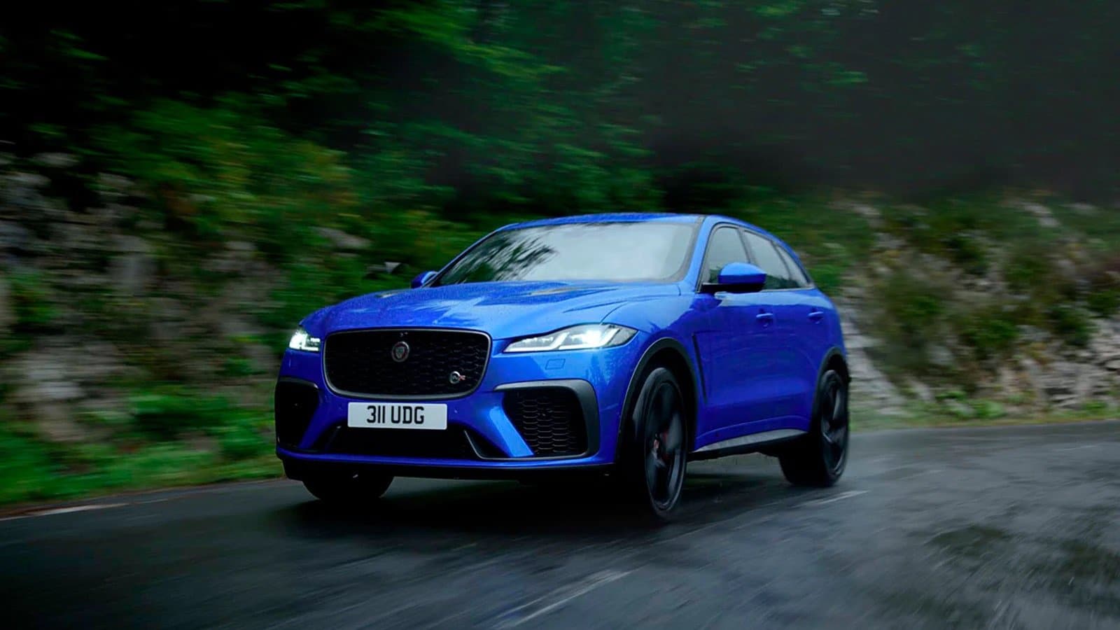 Blue SUV driving on a wet road, surrounded by lush greenery, showcasing dynamic performance.