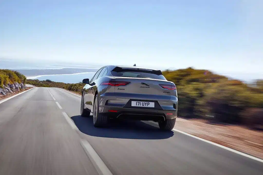 Jaguar I-Pace electric SUV driving on a scenic coastal road under a clear sky.