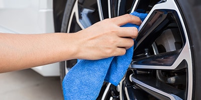 Hand cleaning car wheel rim with blue cloth, showcasing car maintenance and detailing.