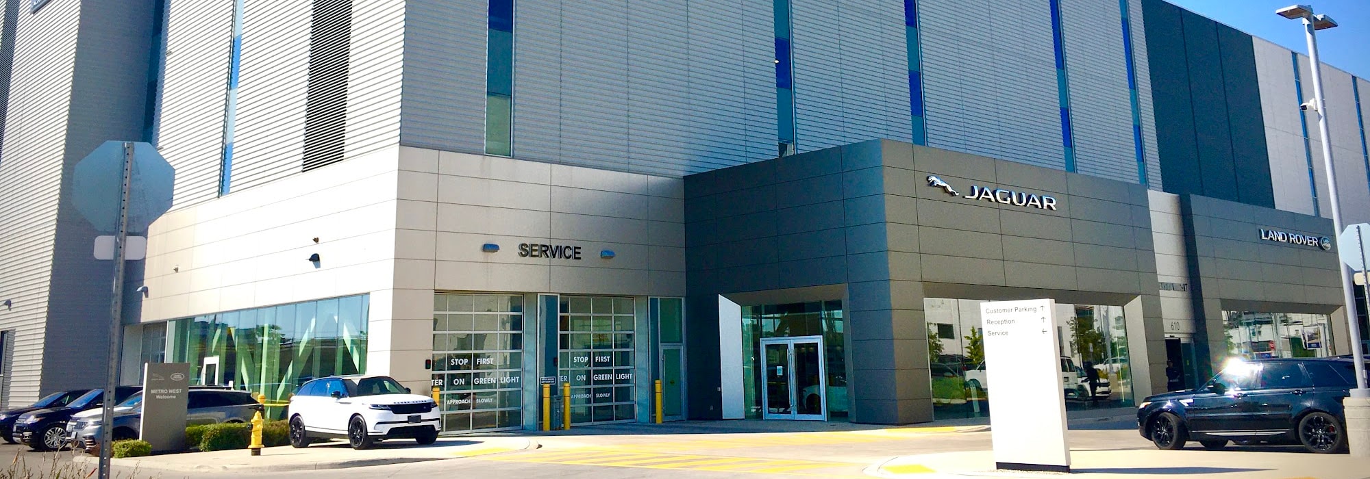 Exterior of a Jaguar Land Rover dealership with service entrance and cars parked outside.